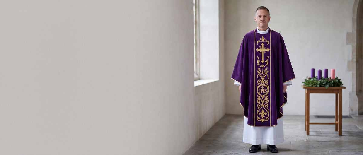 A priest in a deep violet velvet chasuble with a gold IHS and cross orphrey beside an Advent wreath in a stone chapel