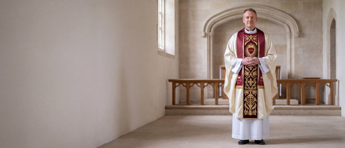 A priest in an ivory chasuble with a burgundy Sacred Heart orphrey and matching stole, standing in a pale stone church