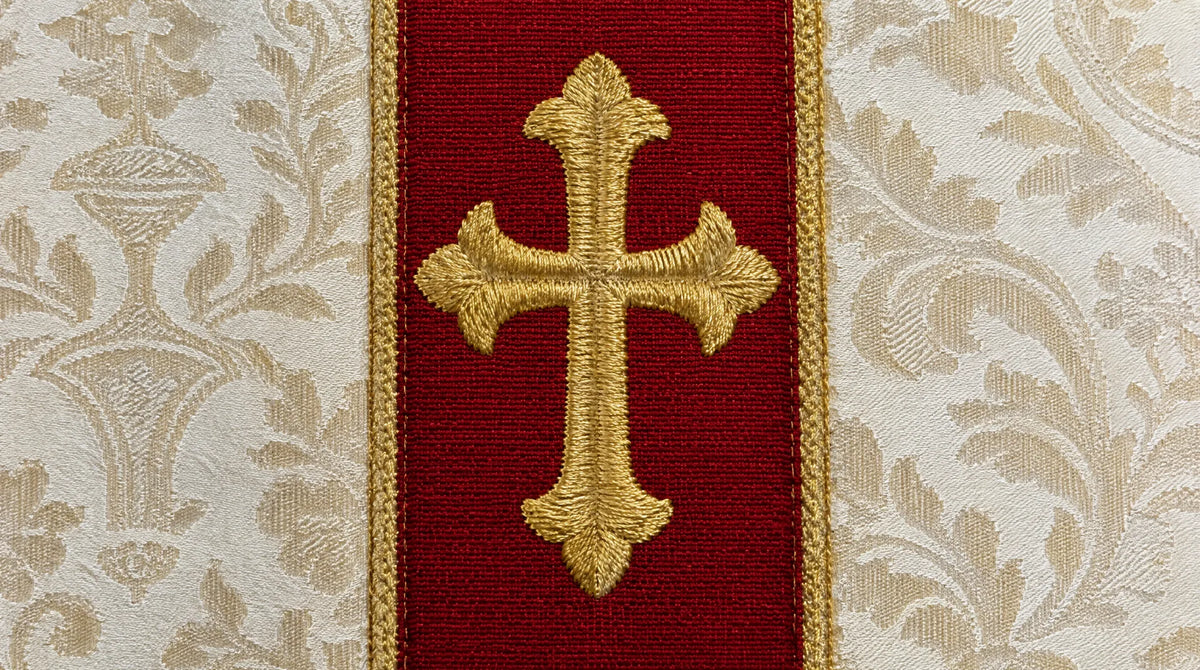 Close-up of a gold satin-stitch embroidered cross on a red orphrey band applied to an ivory damask chasuble