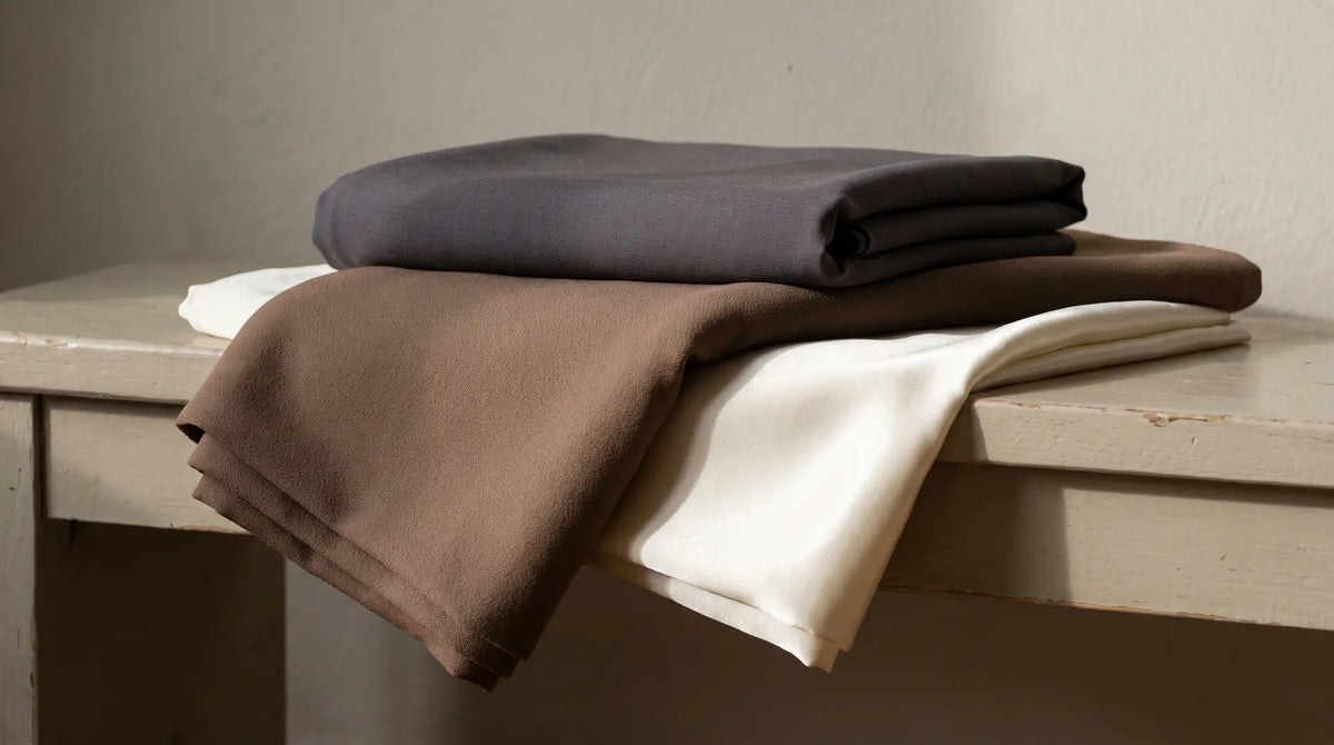 Folded lengths of polyester, wool crepe and silk stacked to show the difference in drape and sheen