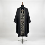 Front of a black damask chasuble with a black velvet column orphrey embroidered in silver with a cross, a lily vine and gothic arches