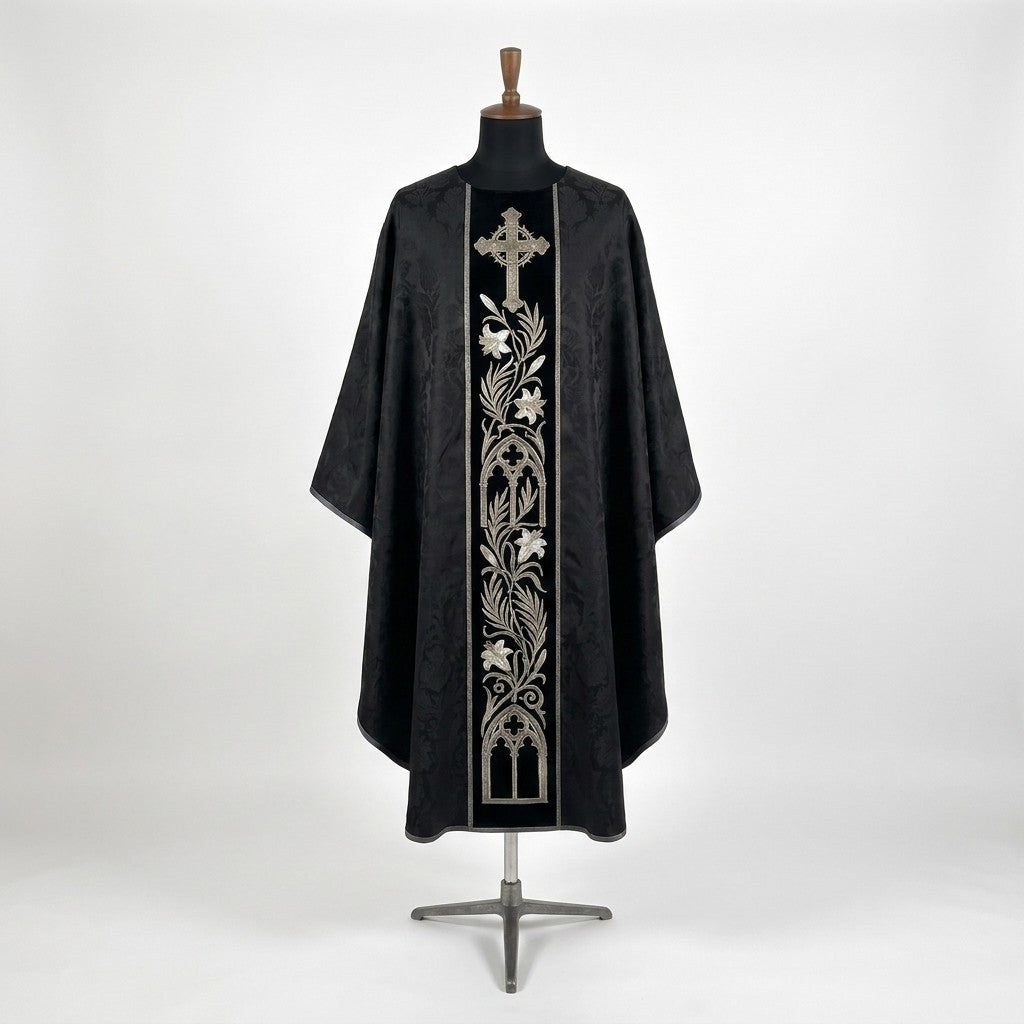 Front of a black damask chasuble with a black velvet column orphrey embroidered in silver with a cross, a lily vine and gothic arches