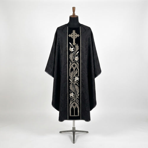 Front of a black damask-pattern chasuble with a black velvet-look column orphrey embroidered in silver with a cross, a lily vine and gothic arches