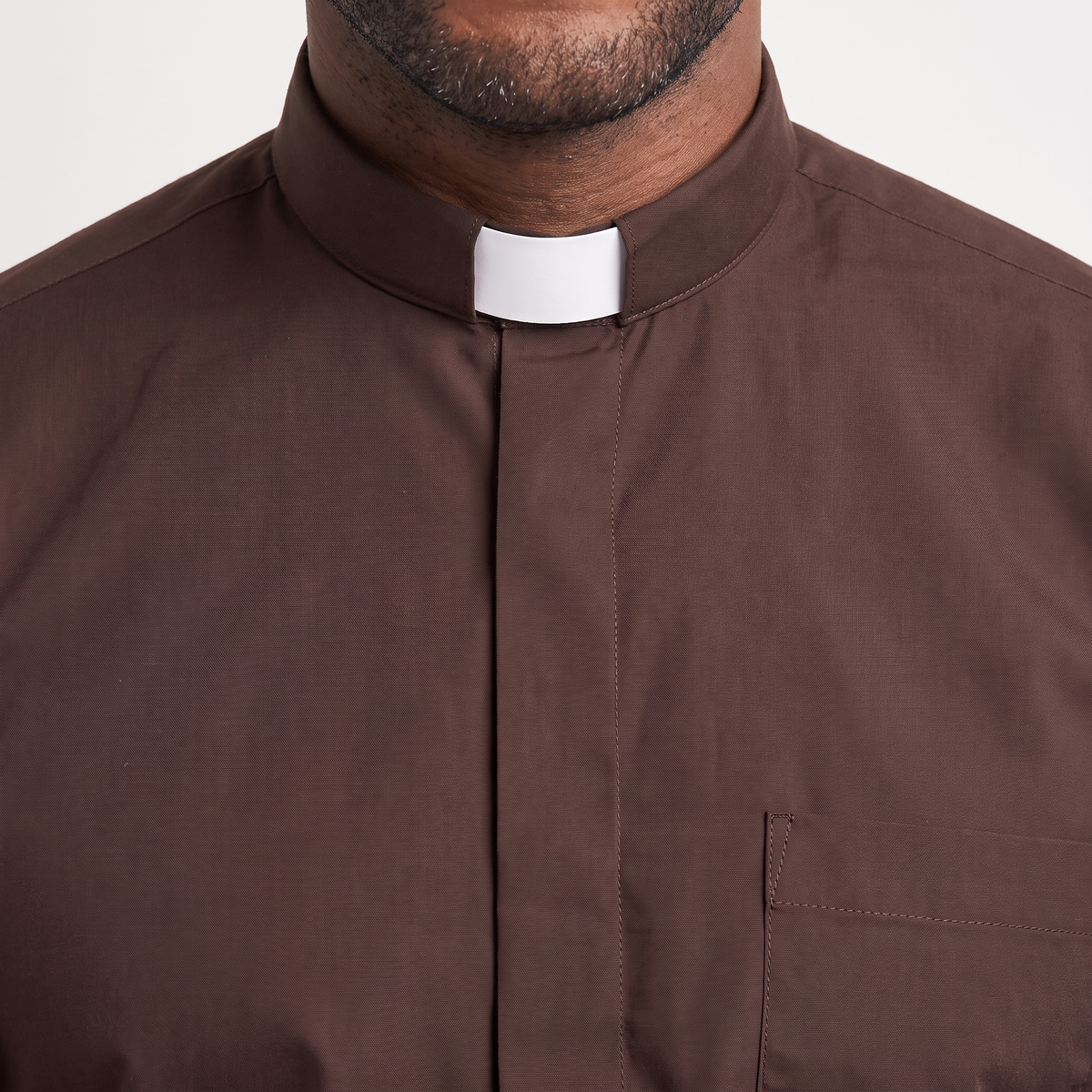 Close-up of the tall brown tab collar with a white tab, the covered button placket and the top of the chest pocket.