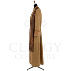 Side view of the camel cassock robe showing the brown yoke, the cuff bands and the flapped hip pocket.