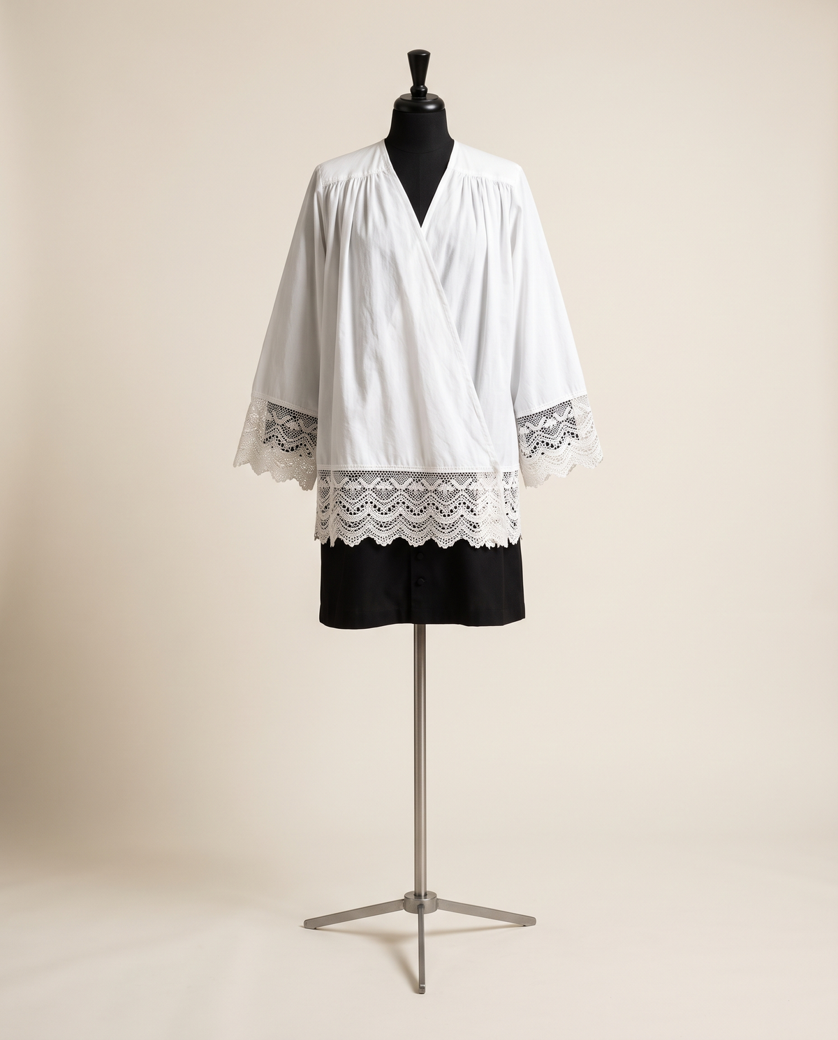 A white cotton surplice with a deep hand-worked lace border worn over a black cassock on a tailor's dress form