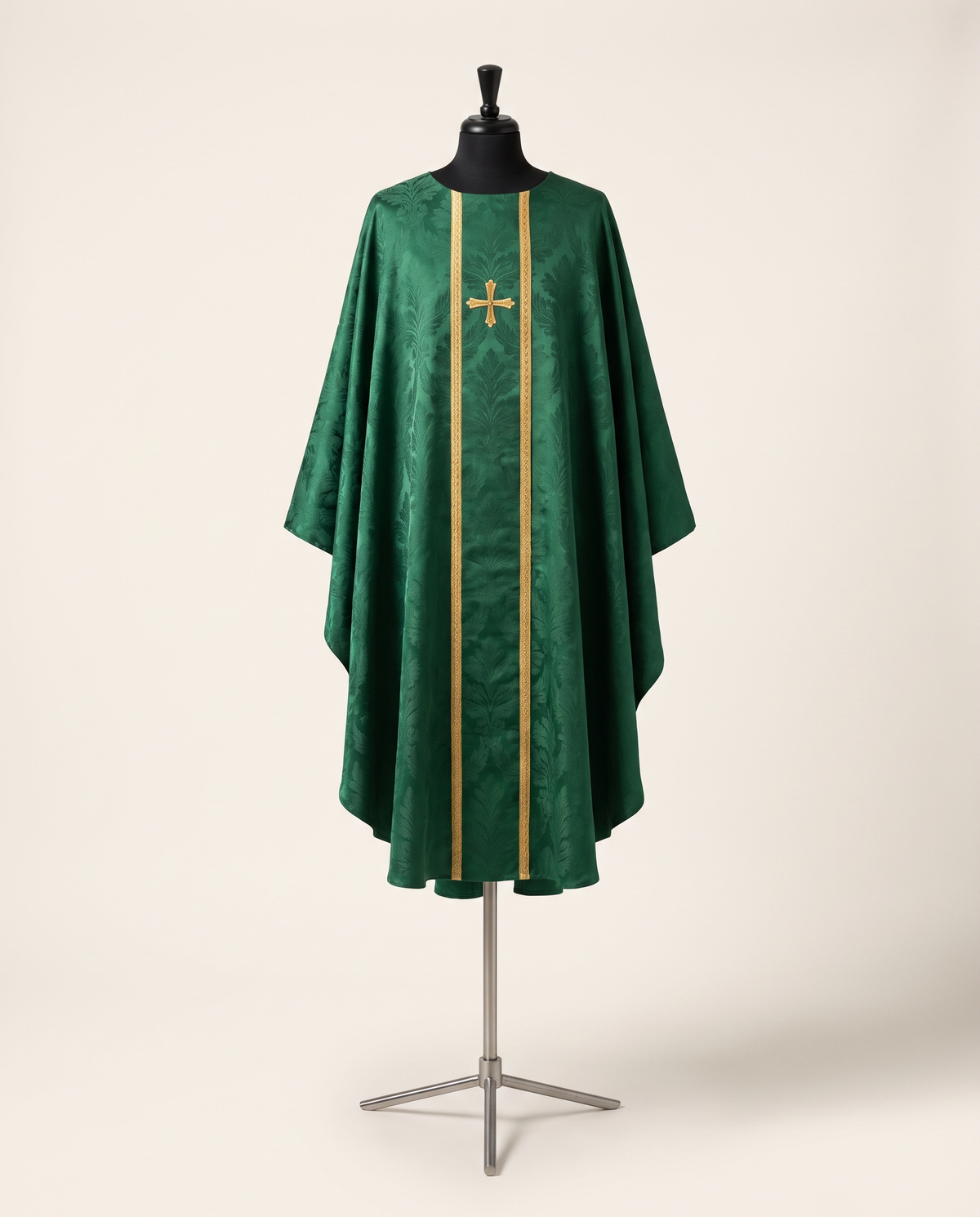 A deep green silk damask Gothic chasuble with a hand-embroidered gold orphrey, shown on a tailor's dress form against a warm off-white studio background