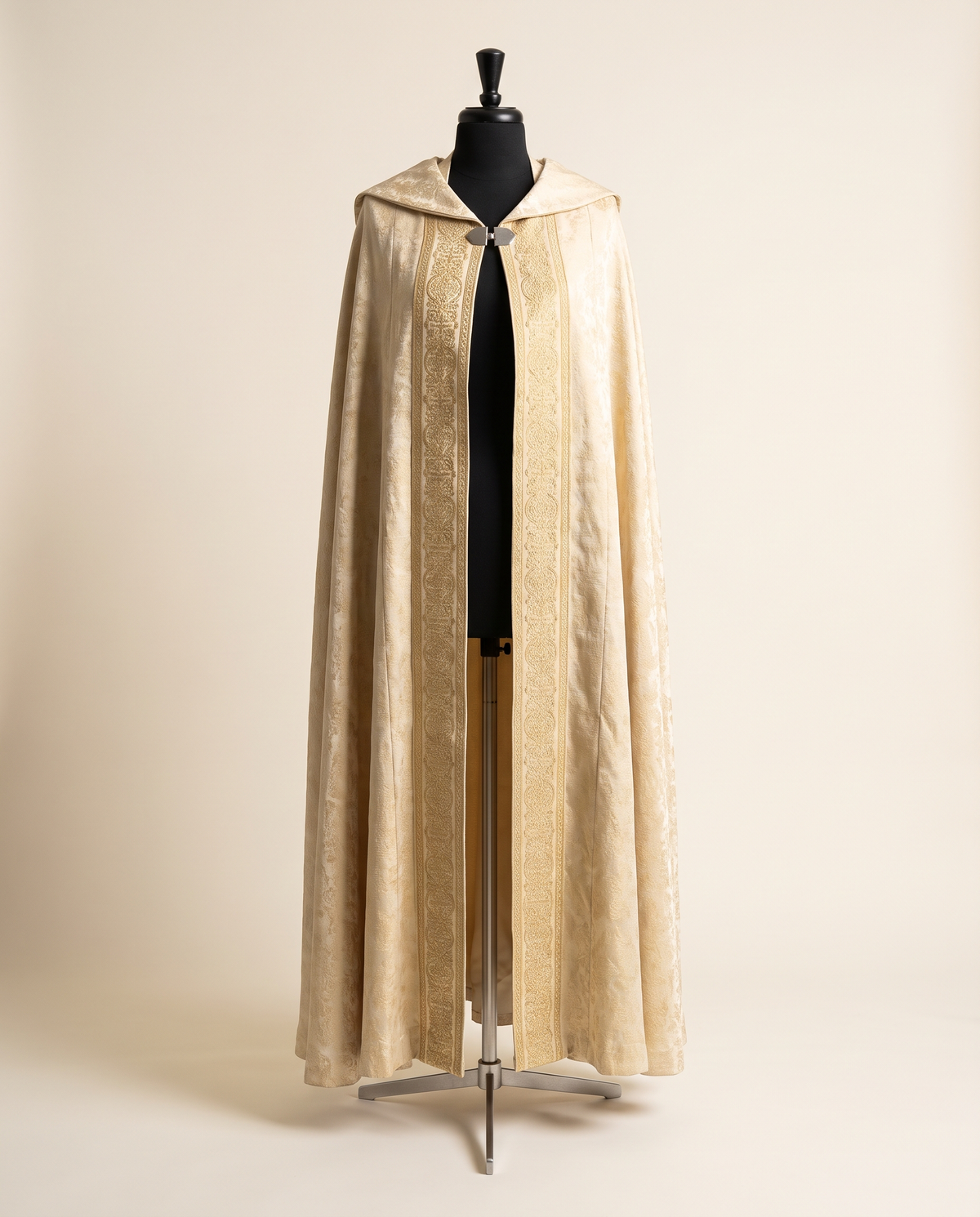 An ivory and gold brocade processional cope with embroidered orphrey bands and a metal morse clasp, shown on a tailor's dress form