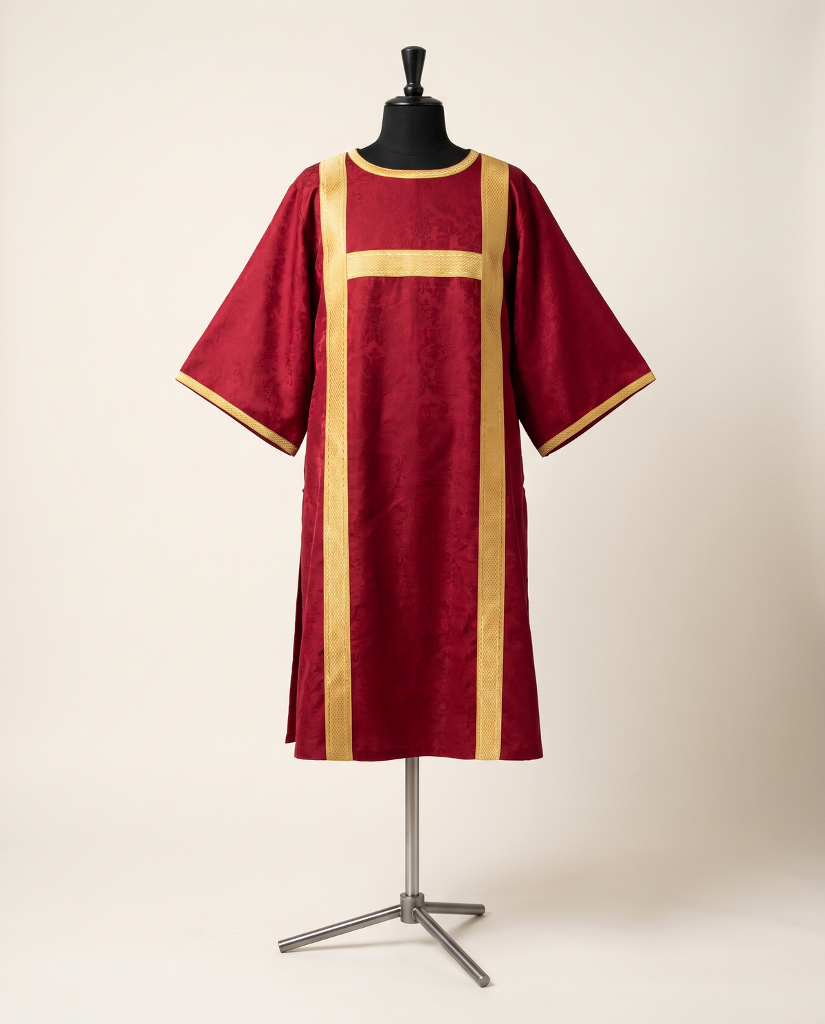 A deacon's dalmatic in red silk damask with wide square sleeves and gold clavi bands, shown on a tailor's dress form