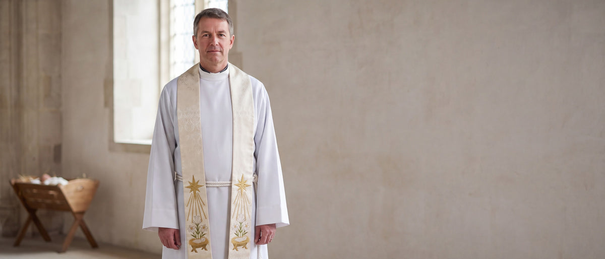 A priest in a white alb wearing an ivory damask Christmas stole embroidered with the Star of Bethlehem, lilies and a manger