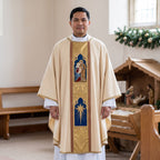 A priest wearing the ivory Holy Family chasuble with gold orphrey panels beside a wooden Nativity crib