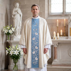 A priest wearing the ivory and Marian blue chasuble with lily vine before a statue of Our Lady and white lilies