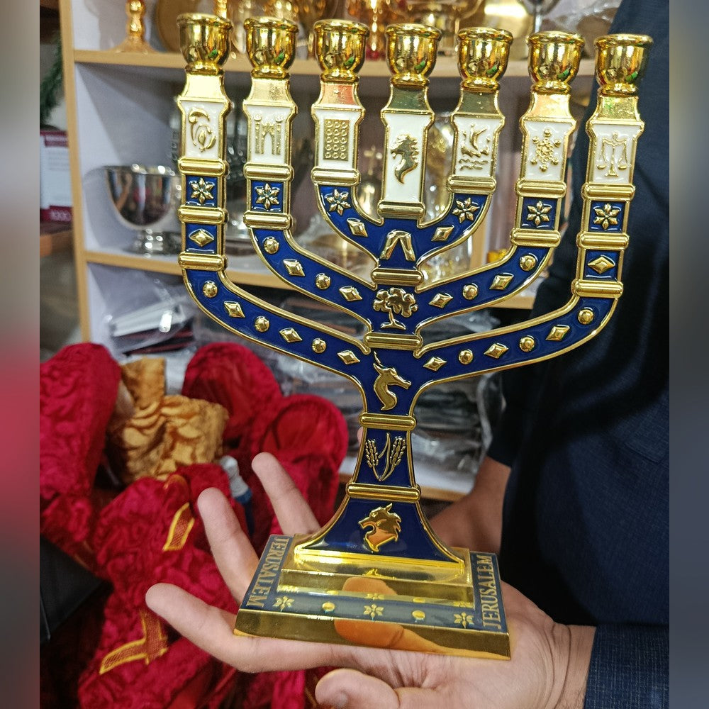 Seven branch Temple menorah in gold-tone metal with deep blue and cream enamel, the twelve tribal emblems on the branches and JERUSALEM lettered on the base, held in the hand to show its size