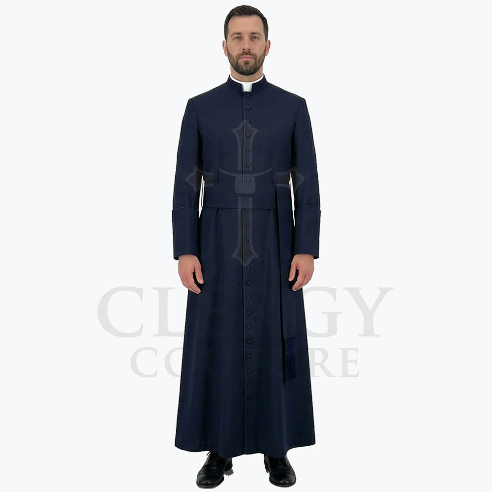 A pastor wearing the navy blue clergy cassock robe, front view, showing the stand collar and the sash belt with tassel.