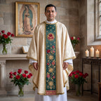 A priest wearing the ivory Guadalupe chasuble with green rose orphrey beneath an image of Our Lady of Guadalupe with red roses and candles