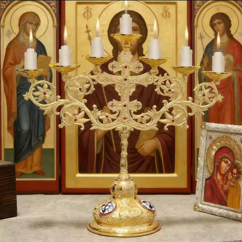Gold seven branch altar candelabra with seven lit candles, standing before icons, with a stone-set cross at the centre and lily scrollwork to either side
